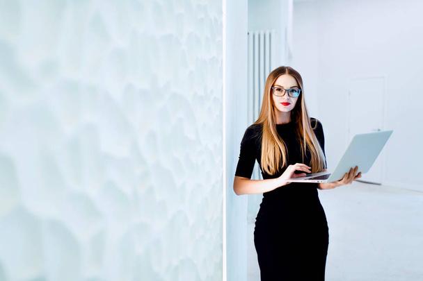 Young business woman holding computer in hands. White office background with copy space. Toned - Foto, imagen
