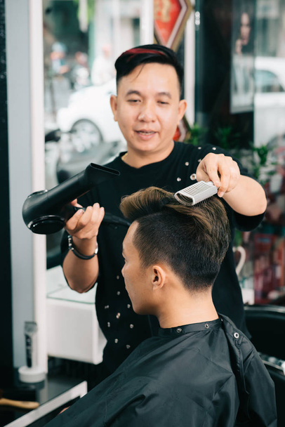 professioneller Friseur mit spezieller Bürste und Ventilator, um die Haare seiner Kunden richtig zu trocknen - Foto, Bild