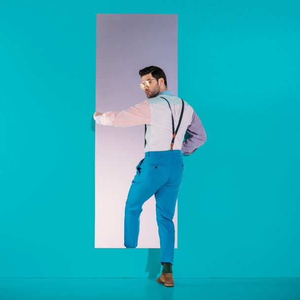 rear view of handsome man in fashionable clothes going through frame on turquoise - Foto, Imagen