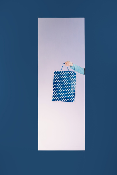 περικομμένη εικόνα κοπέλα που κρατά την τσάντα για ψώνια σε απομονωμένη στο μπλε πλαίσιο - Φωτογραφία, εικόνα