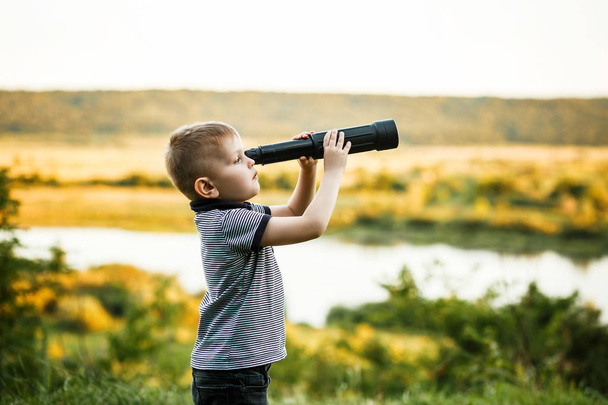 Menino loiro olhando no telescópio no fundo do parque de verão
 - Foto, Imagem