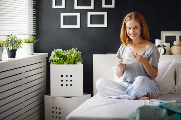 Szczęśliwa młoda kobieta z kubkiem porannej kawy w łóżku - Zdjęcie, obraz