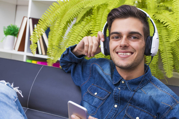young man listening to music in the home Lounge with phone and earphones - Foto, afbeelding