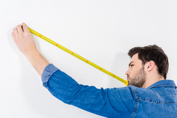 hombre que mide la pared con cinta métrica en blanco
 - Foto, Imagen