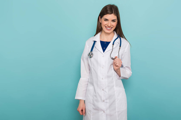 Selbstbewusste junge Ärztin mit Stethoskop blickt vor blauem Hintergrund in die Kamera  - Foto, Bild
