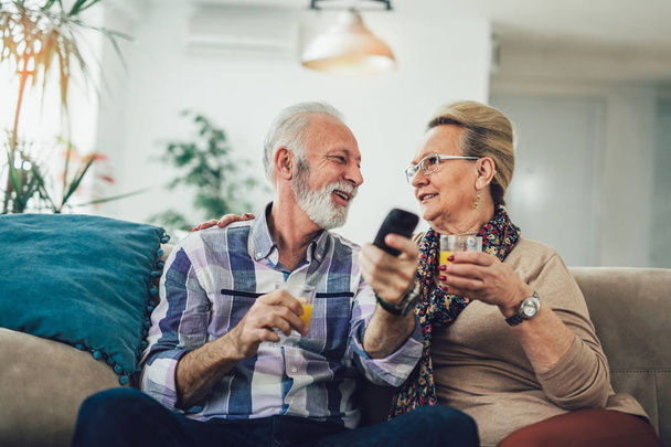 Happy senior couple with remote control watching tv on couch - Фото, зображення