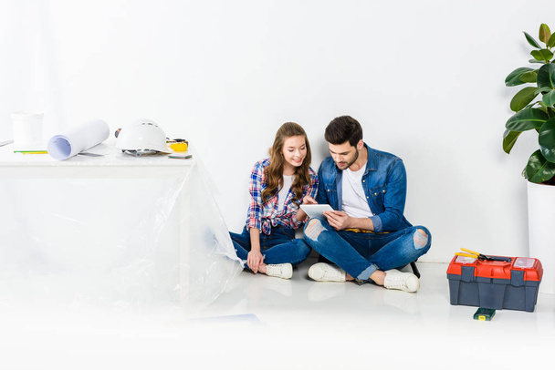 smiling couple sitting on floor and using tablet - Φωτογραφία, εικόνα