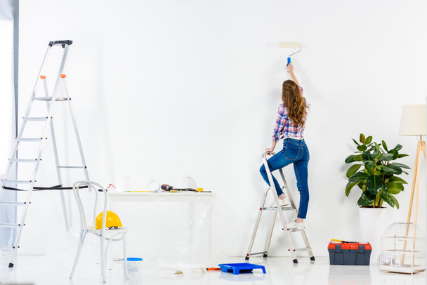 rear view of girl standing on ladder and painting wall - Photo, Image