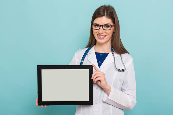 Confident young female doctor with stethoscope holding empty frame  - Fotó, kép
