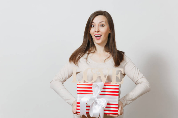 Mooie jonge sexy lachende vrouw met rode aanwezig doos met cadeau, houten woord liefde op witte achtergrond. Kopiëren van ruimte voor reclame. St. Valentine's Day of International Women's Day concept. - Foto, afbeelding