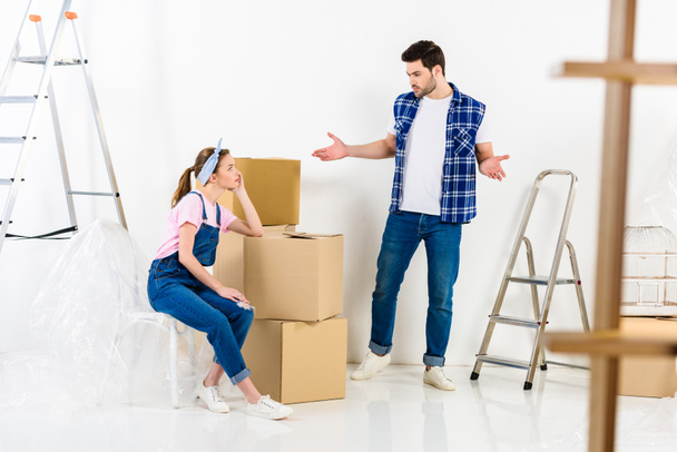 boyfriend showing shrug gesture and looking at girlfriend sitting on boxes - Photo, Image