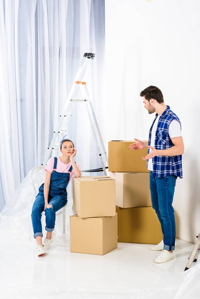 boyfriend showing shrug gesture and looking at girlfriend sitting on boxes - Photo, Image