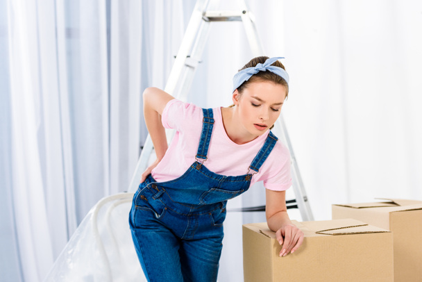 girl with pain in back after moving heavy boxes - Foto, afbeelding