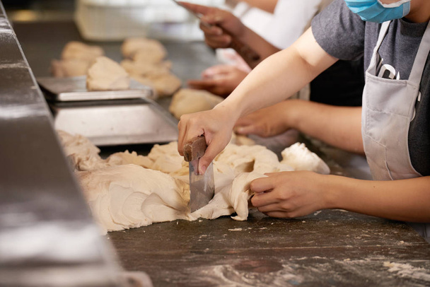 Hands of chef cutting piece of dough with scrapper knife - Фото, зображення