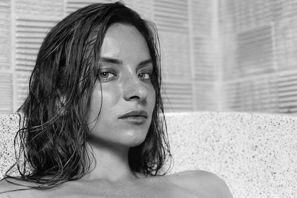Highly detailed close up shot of mixed race beautiful model with green eyes and wet brunette hair taking bath on private villa, looking mystically at camera. Black and white image of  natural face. - Photo, Image
