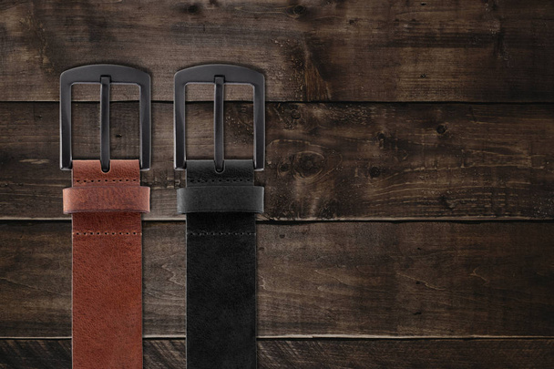 brown and black men's leather belts on wooden background. men's fashionable large belts on the brown table. top view of men's belts background with copy space - 写真・画像