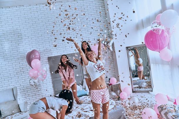 happy attractive young women in pajamas jumping in bedroom with confetti and balloons - 写真・画像