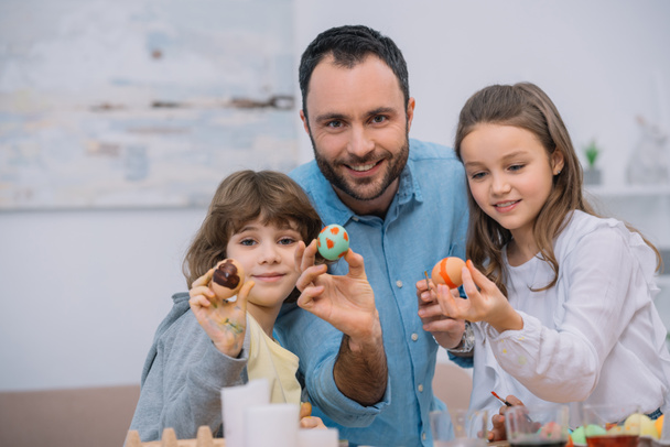 isä ja lapset osoittavat pääsiäismunia kamerassa
 - Valokuva, kuva