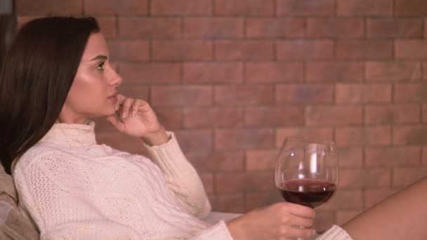 Young woman sitting at home by the fireplace and drinking a red wine. - Filmati, video