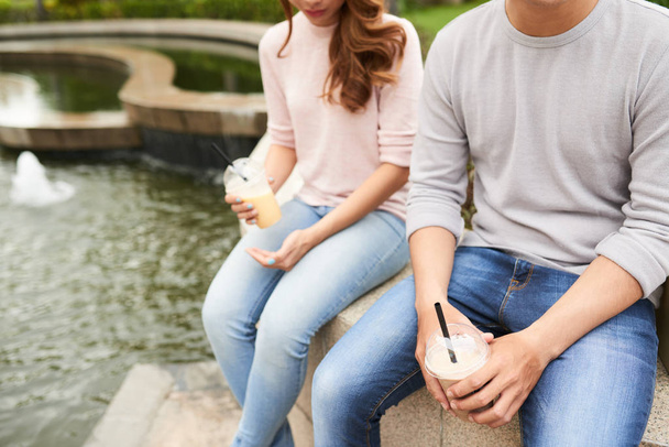 Imagen recortada de pareja sentada junto a la fuente y disfrutando de cócteles de leche
 - Foto, Imagen