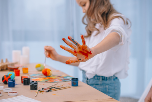 little child showing colorful dirt hand while painting eggs - Fotó, kép