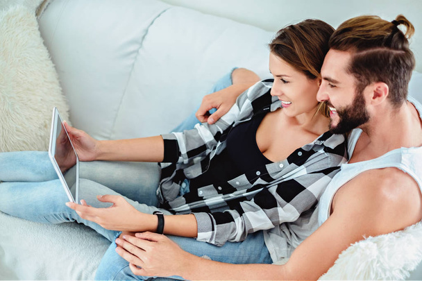 Ζευγάρι ψάχνει στο tablet στον καναπέ και χαμογελαστός - Φωτογραφία, εικόνα