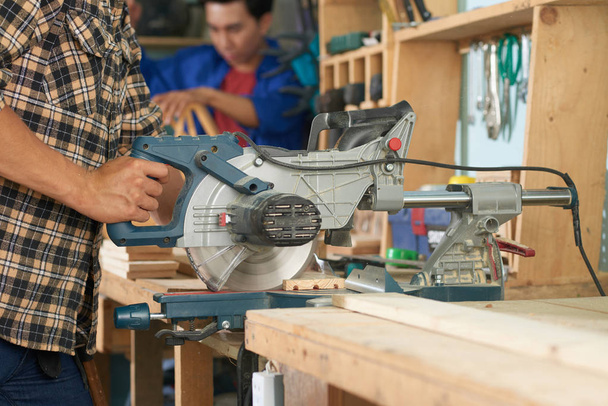 Manos de carpintero cortando madera con sierra eléctrica
 - Foto, Imagen