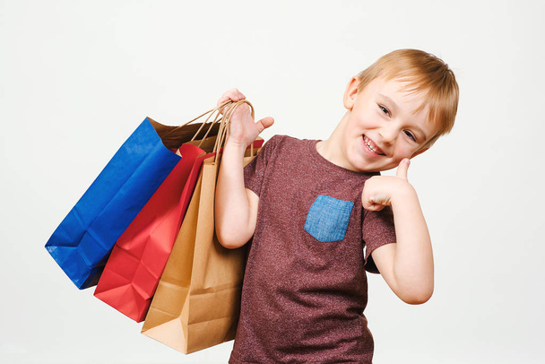 Χαριτωμένο ευτυχισμένο παιδί με πολύχρωμες τσάντες για ψώνια στο λευκό φόντο. - Φωτογραφία, εικόνα