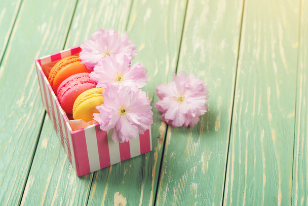 Gift box with three french macaroons and sakura flowers on wooden background. Copy space. Selective focus. - Photo, Image