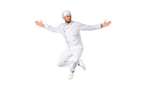 young male chef in uniform jumping with open arms isolated on white - Фото, изображение