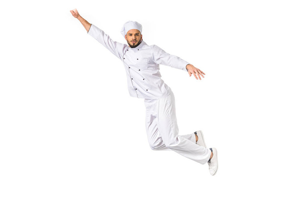 young male chef with raised hand flying and looking at camera isolated on white - 写真・画像