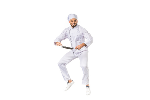 happy young chef holding frying pan while jumping and smiling at camera isolated on white   - Foto, Bild
