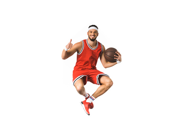 happy young basketball player holding ball and showing thumb up isolated on white - Fotó, kép