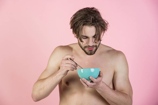 Morning, vegetarian, organic food. Dieting and fitness, calorie. Sexy man with muscular body eating cereal, healthcare. Man with wet hair eat breakfast on pink background. Food and beauty, health. - Foto, afbeelding