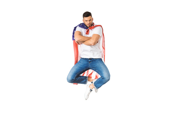 handsome young man with american flag jumping with crossed arms and looking at camera isolated on white - 写真・画像