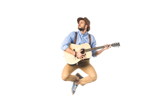 romantic young musician looking away while playing guitar and jumping isolated on white - Valokuva, kuva