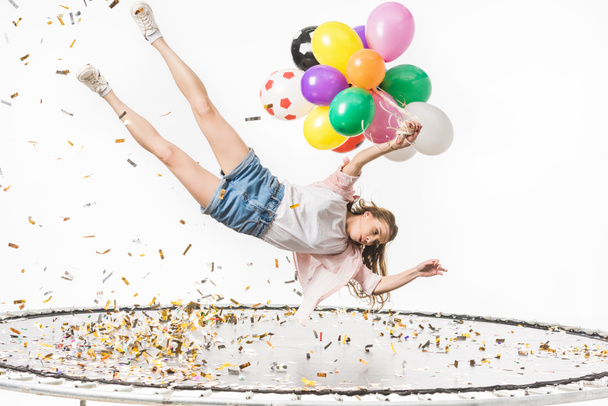 girl holding colorful balloons and falling on trampoline isolated on white  - Foto, immagini