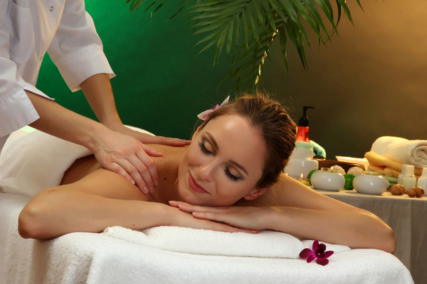 красивая женщина в спа салон с камнями получать массаж, на зеленом фоне
 - Фото, изображение