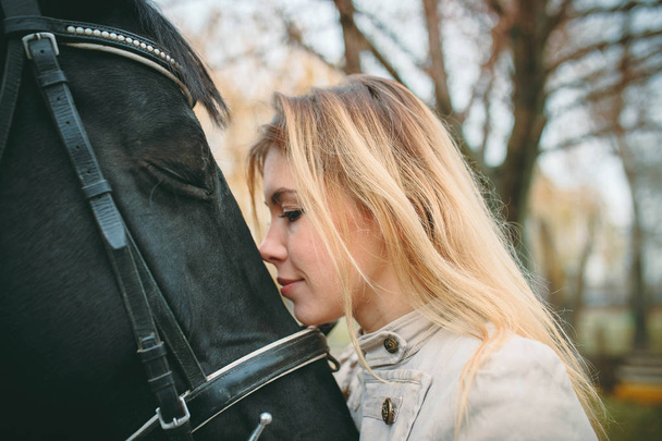Portrait of a blonde woman with a black horse - Photo, Image