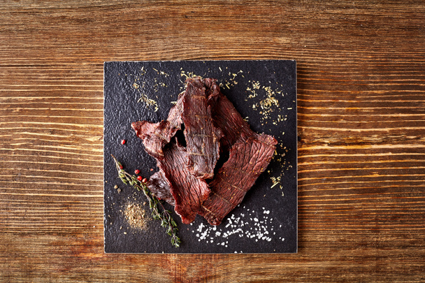 Carne seca picada cortada en tiras en el tablero negro sobre fondo de madera
 - Foto, imagen