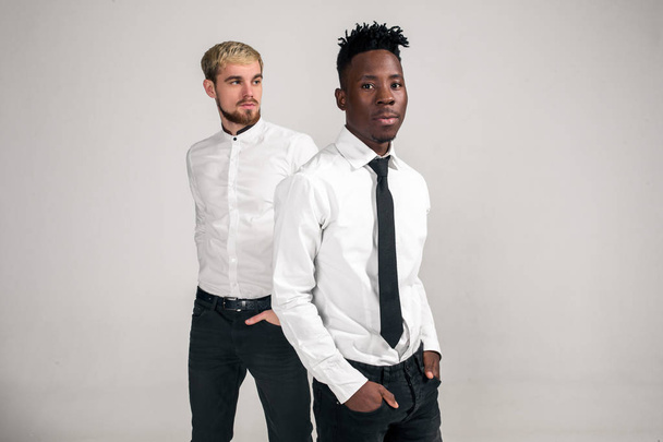 Friends. Two guys in white shirts and dark pants posing in the studio on a white background - Foto, Imagem
