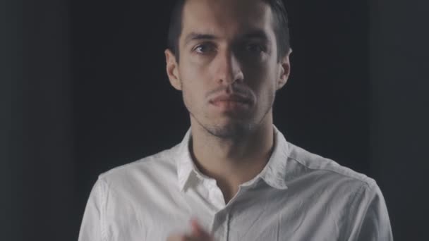junger attraktiver Mann in weißem Hemd blickt vereinzelt in die Kamera auf schwarzem Hintergrund - Filmmaterial, Video