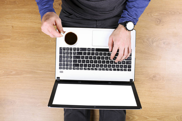 Мужчина блоггер серфинг Интернет, блоги, онлайн покупки на компьютере ноутбука и мобильного телефона, пить черный кофе, учеба. Молодой человек над головой круги, джинсы синий длинный рукав, деревянный текстурированный пол
. - Фото, изображение