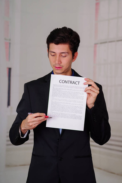 Close up of boss wearing a suit and giving a sheet of paper of contract text on it, and holding a pen to sign the document, in a blurred background - Foto, afbeelding