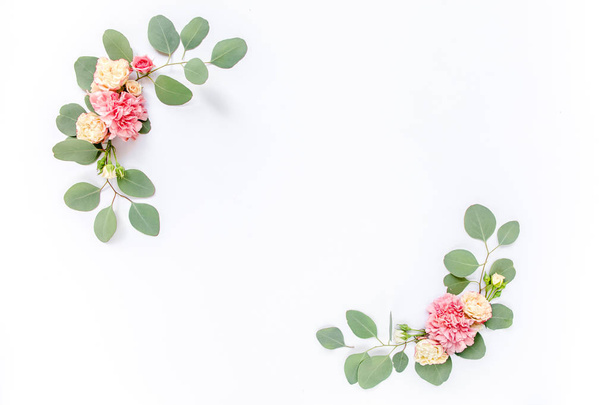 Beautiful roses and carnations buds, branches of eucalyptus and leaves border frame, isolated on white background. The apartment lay, top view. - Fotó, kép