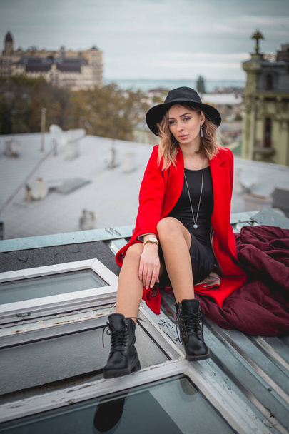 Dívka v červené barvě a s černým kloboukem pózuje na střechy starého města - Fotografie, Obrázek