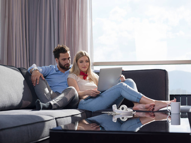Young couple relaxing at luxury home using laptop computer reading in the living room on the sofa couch. - Foto, imagen