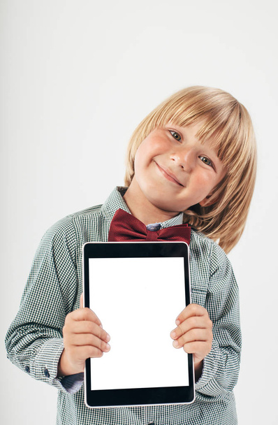Smiling School boy in shirt with red bow tie, holding tablet computer in white background - 写真・画像
