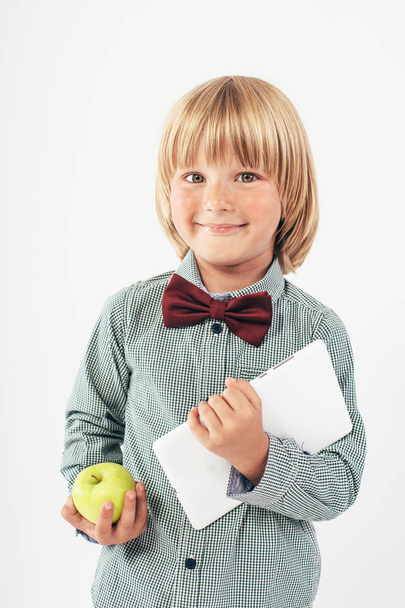 Smiling School boy in shirt with red bow tie, holding tablet computer and green apple in white background - Foto, Imagen