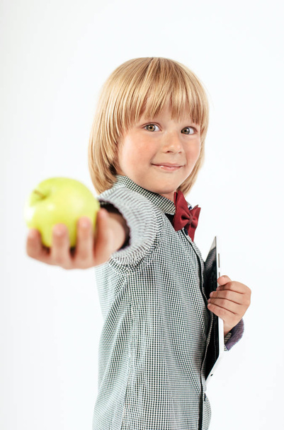 Smiling School boy in shirt with red bow tie, holding tablet computer and green apple in white background - Photo, Image